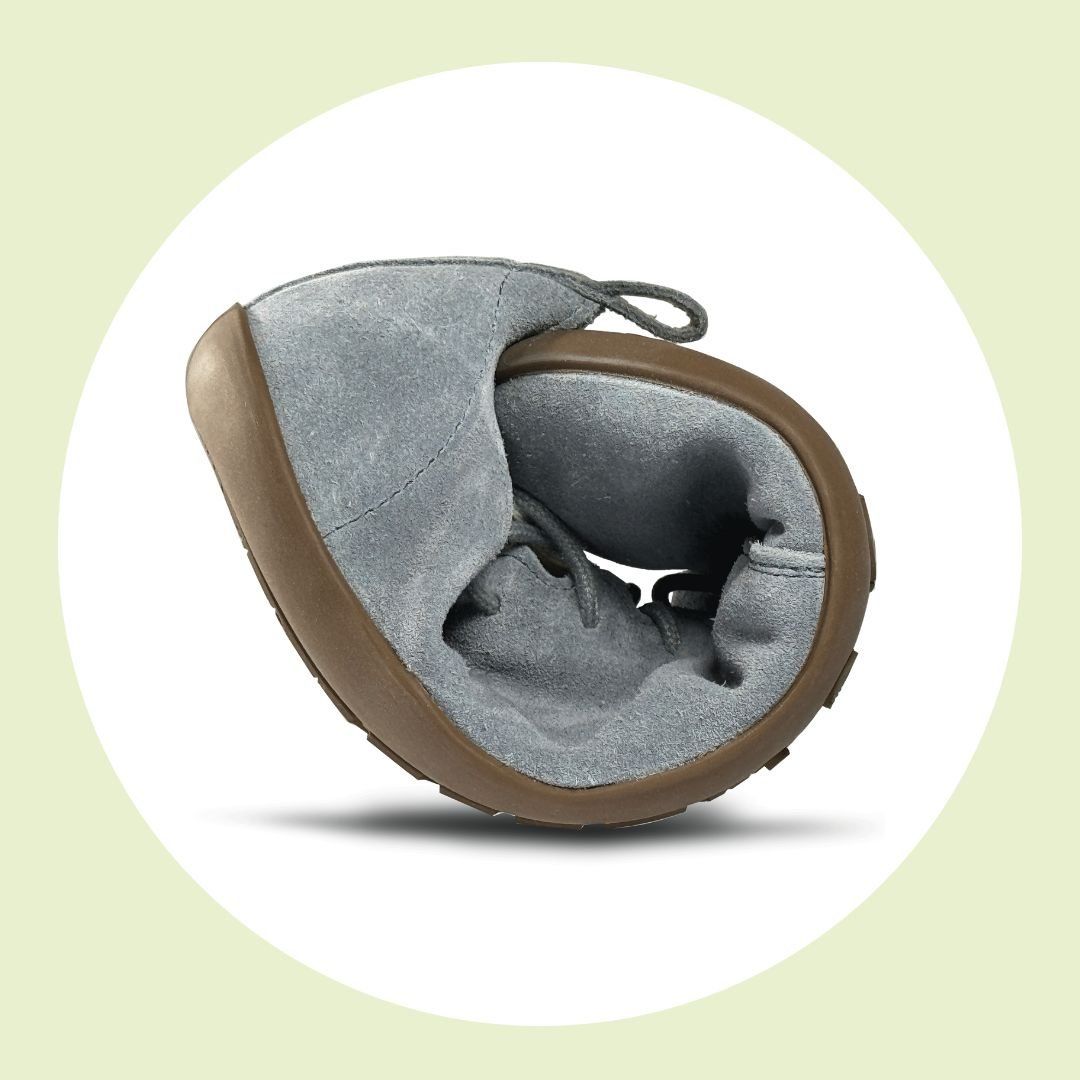 Ein graublauer, flexibler Kinderschuh, der zusammengerollt ist und die weiche Ledersohle zeigt