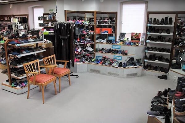 Verschiedene Sportschuhe und Accessoires in einem Schuhgeschäft Innenansicht eines Schuhgeschäfts mit einer großen Auswahl an Sportschuhen, Regalen voller Schuhe und Accessoires sowie zwei Stühlen im Vordergrund.