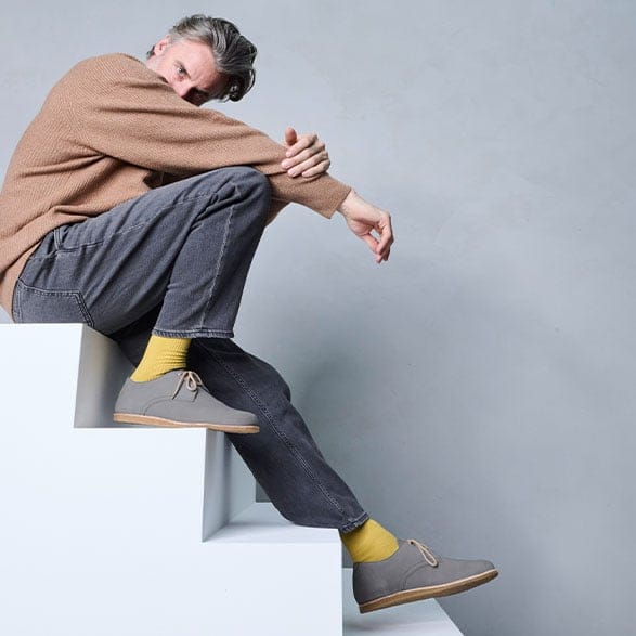 Man in brown sweater and grey pants with yellow socks and grey shoes sitting on white stairs