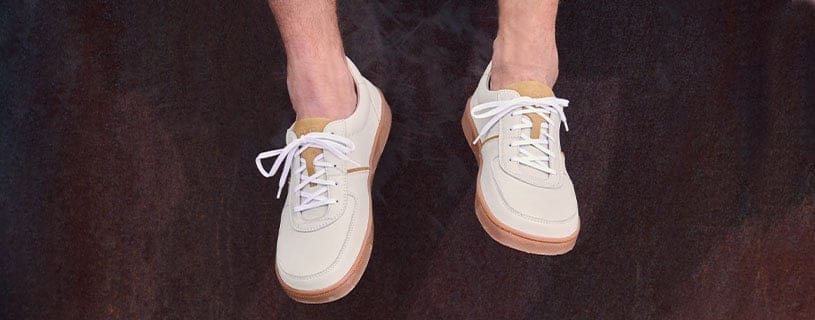 Moderne beige Sneaker mit weißer Sohle Beige Sneaker mit weißer Sohle und Schnürsenkeln, getragen von einer Person vor dunklem Hintergrund