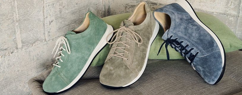 Modische Wildlederschuhe in Grün, Beige und Blau Drei Paar Wildlederschuhe in verschiedenen Farben: Grün, Beige und Blau, auf einem Stoffkissen arrangiert