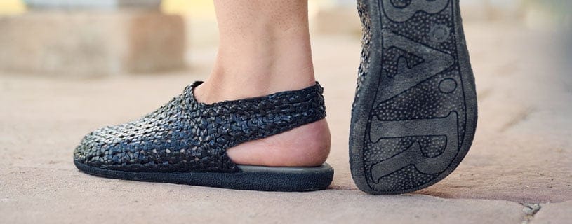 Bequeme handgefertigte Slipper aus geflochtenem Material Nahaufnahme von Füßen in handgefertigten, geflochtenen Slippern auf Steinboden