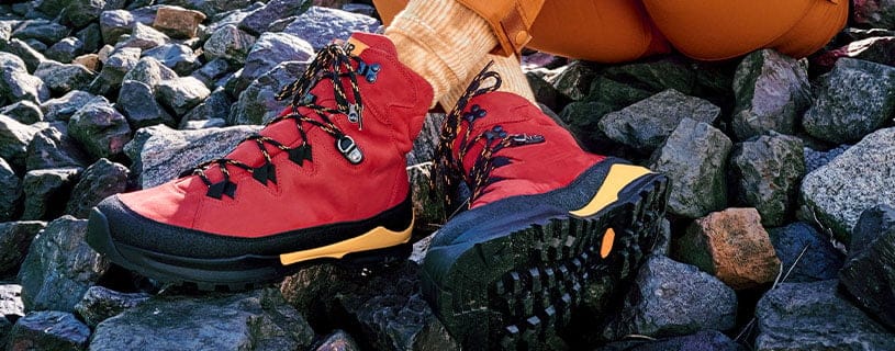 Rote Outdoor-Wanderschuhe auf felsigem Untergrund Nahaufnahme von roten Wanderschuhen mit robuster Sohle auf steinigem Boden