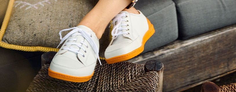 Modische weiße Sneaker mit orangefarbener Sohle Weiße Sneaker mit orangefarbener Sohle auf einem geflochtenen Hocker