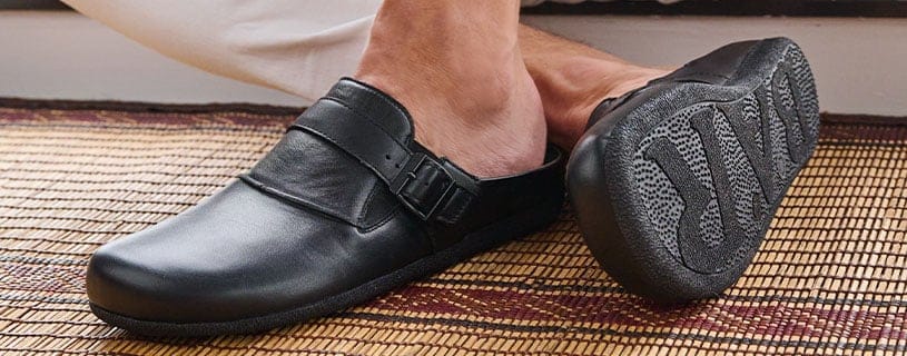 Schwarze Herrenslipper aus Leder mit ergonomischer Sohle Ein schwarzer Herrenslipper aus Leder mit ergonomischer Sohle auf einer geflochtenen Matte