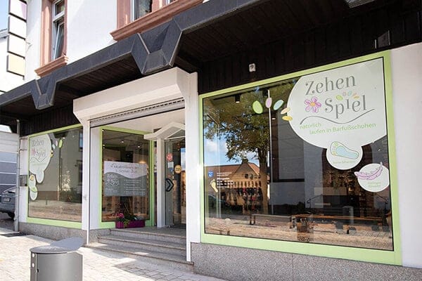 Eingangsbereich des Zehen Spiel Barfußschuhladens Außenansicht des Zehen Spiel Barfußschuhladens mit Schaufenster und Logo