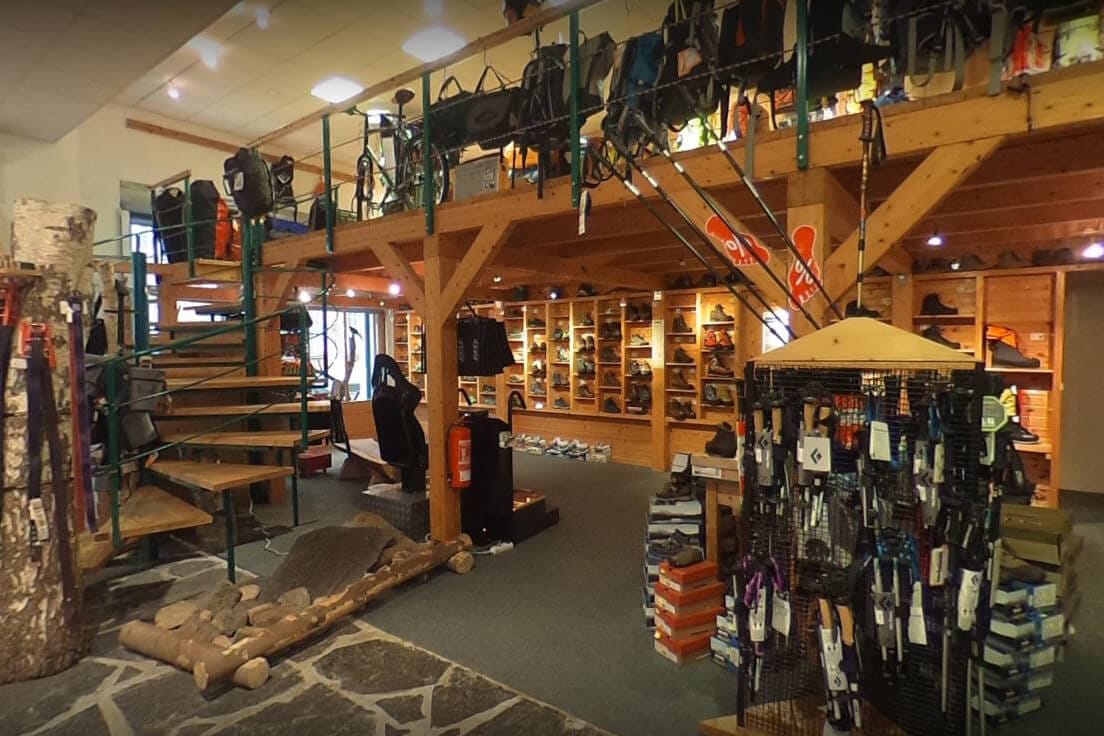 Outdoor-Ausrüstungsgeschäft mit breiter Auswahl an Rucksäcken und Wanderschuhen Innenraum eines Outdoor-Geschäfts mit Holzregalen voller Wanderschuhe, Treppenaufgang und diversen Rucksäcken