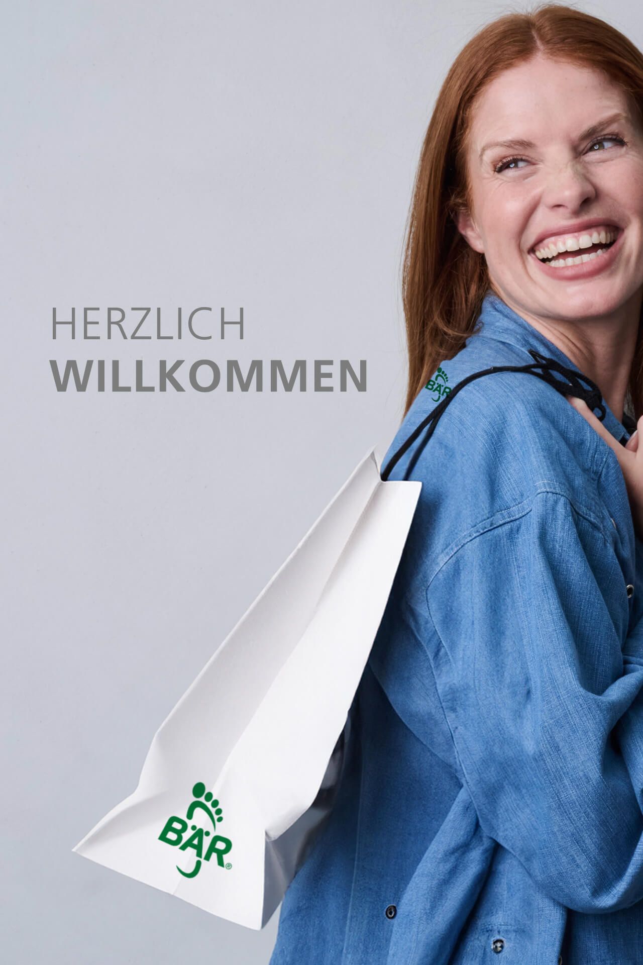 Frau in blauer Bluse lächelt mit Einkaufsbeutel auf der Schulter und Aufschrift 'Herzlich Willkommen'