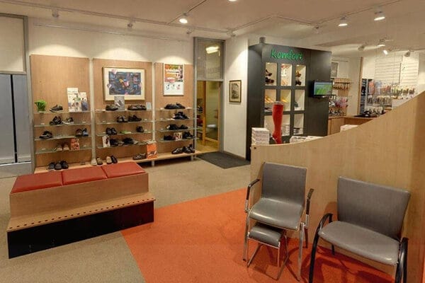 Innenansicht eines Schuhgeschäfts mit modernen Regalen und Sitzgelegenheiten Ein Schuhgeschäft mit modernen Regalen voller Schuhe, roten Sitzbänken und grauen Stühlen auf rotem Teppichboden.
