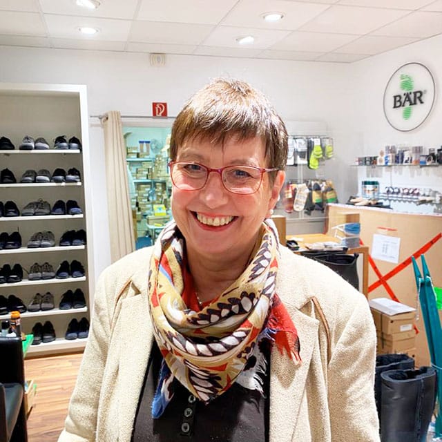 Freundliche Verkäuferin in einem Schuhgeschäft Eine lächelnde Frau mit Brille und buntem Schal in einem Schuhgeschäft