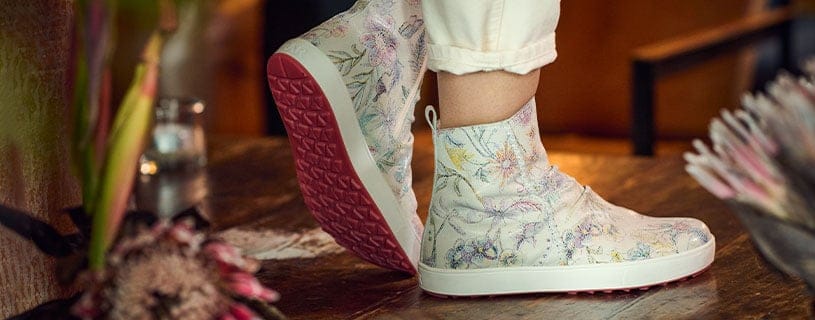 Modische Ankle Boots mit floralem Muster und rosa Sohle Person trägt Ankle Boots mit Blumenmuster und rosa Sohle auf Holzboden