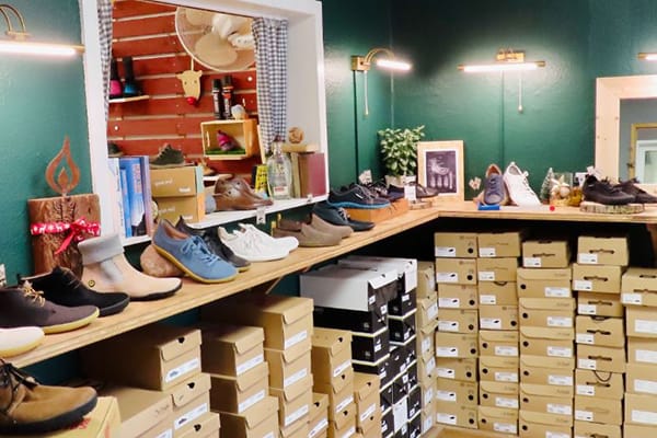 Verschiedene Schuhe auf einem Holzregal in einem Schuhladen, umgeben von zahlreichen Schuhkartons.