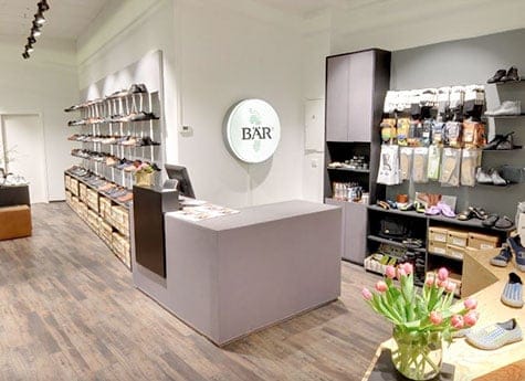 Moderner Schuh- und Accessoire-Laden mit heller Einrichtung Innenansicht eines modernen Schuhladens mit Regalen voller Schuhe und Accessoires, einem grauen Tresen und einem Blumenstrauß auf einem Tisch