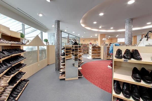 Moderner Schuhshop mit vielfältigem Angebot Innenansicht eines modernen Schuhshops mit einer großen Auswahl an Schuhen für Herren und Damen auf Regalen. Elegante Beleuchtung und roter Teppich heben das Ambiente hervor.