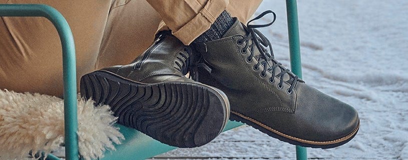 Moderne schwarze Lederstiefel auf blauem Metallstuhl im Freien Person trägt schwarze Lederstiefel und sitzt auf einem blauem Stuhl im Schnee