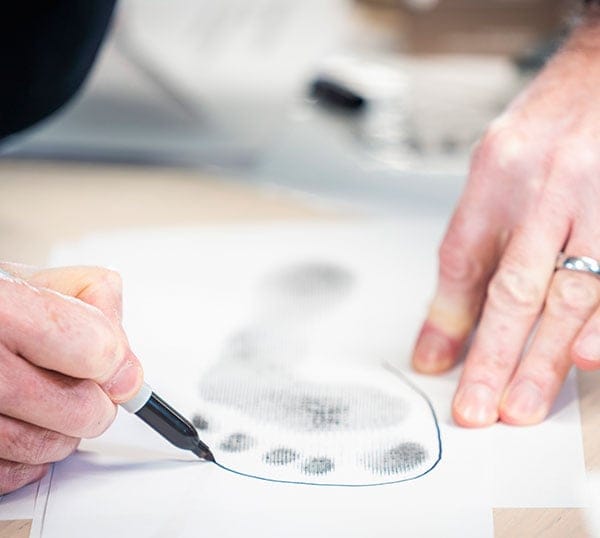 Person zeichnet Umriss eines Fußabdrucks auf Papier Nahaufnahme einer Person, die mit einem Stift den Umriss eines Fußabdrucks auf einem Blatt Papier zeichnet