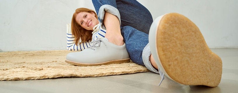 Bequeme Freizeitschuhe für Damen Frau in lässigen Schuhen auf einem Teppich liegend, trägt Jeans und gestreiftes Oberteil