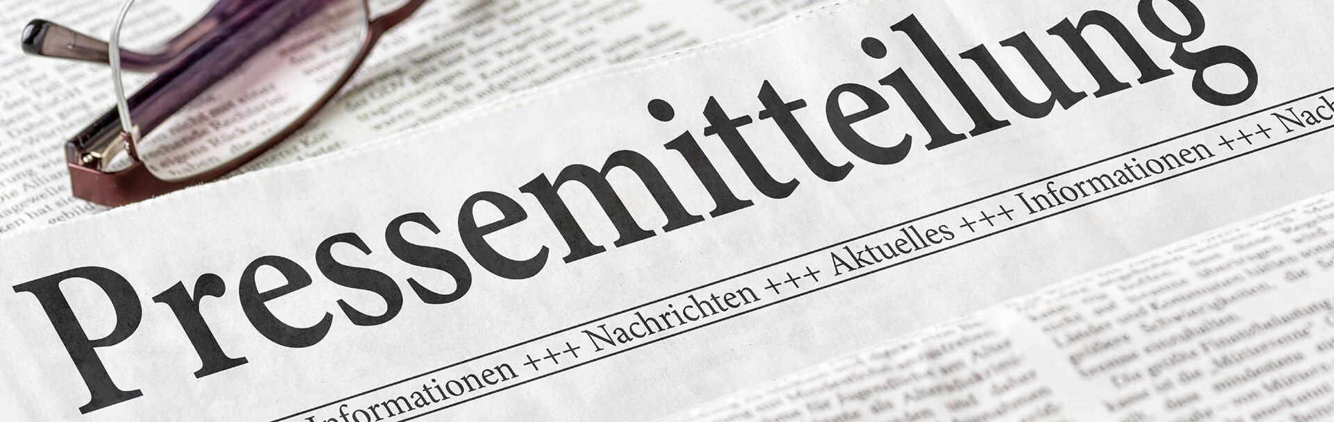 Zeitungsartikel mit dem Titel 'Pressemitteilung' und Lesebrille im Vordergrund Nahaufnahme einer Zeitung mit der Überschrift 'Pressemitteilung' und einer Brille darauf