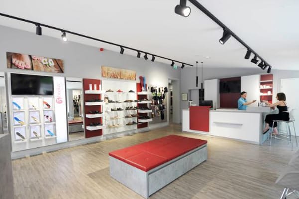 Innenansicht eines modernen Schuhladens mit elegantem Design, beleuchteten Regalen voller Schuhe und einem Verkaufsbereich mit zwei Personen.
