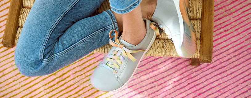 Damen-Sneaker mit farbigen Schnürsenkeln Person in Jeans und Sneakers mit farbigen Schnürsenkeln auf einem Korbstuhl