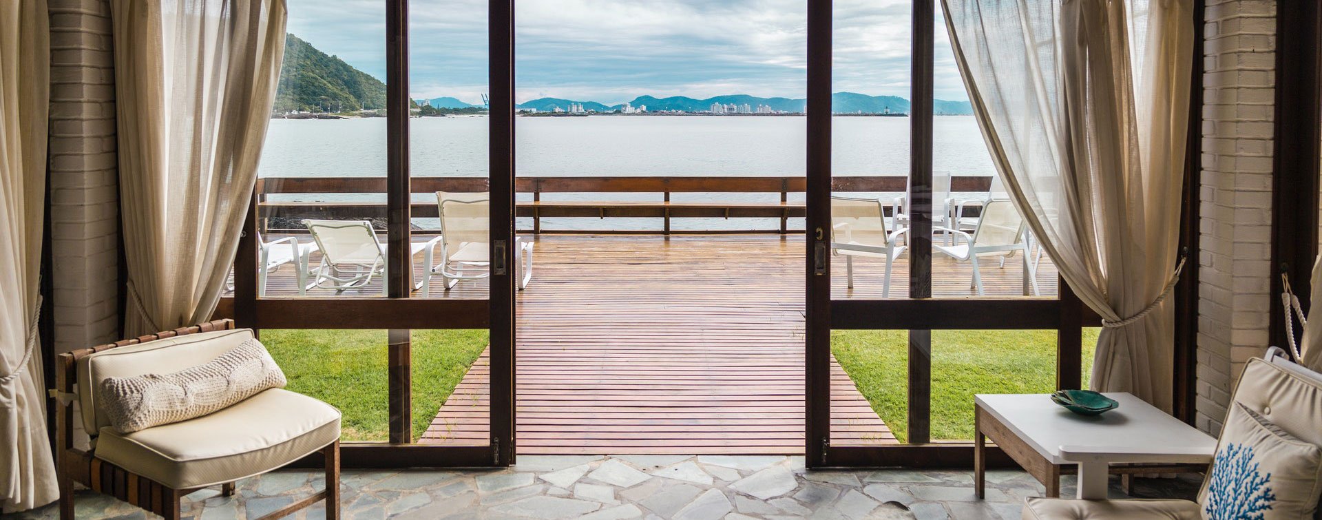 Gemütliche Terrasse mit Meerblick und eleganter Einrichtung Gemütliche Terrasse mit Blick aufs Meer, elegant eingerichtetes Zimmer mit Vorhängen und Sitzgelegenheiten