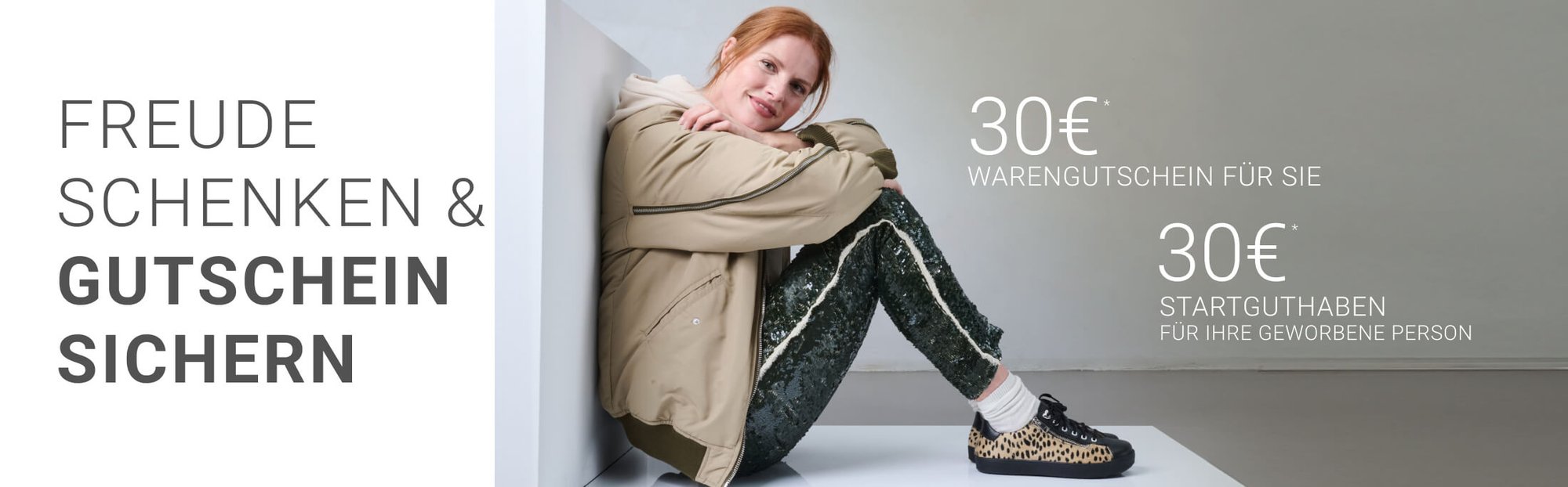 Freude schenken und Gutschein sichern – 30€ Warengutschein für Sie und 30€ Startguthaben für Ihre geworbene Person Frau sitzt in moderner Kleidung und vermittelt den Text 'Freude schenken & Gutschein sichern', mit Angeboten von 30€ Warengutschein und 30€ Startguthaben für geworbene Personen