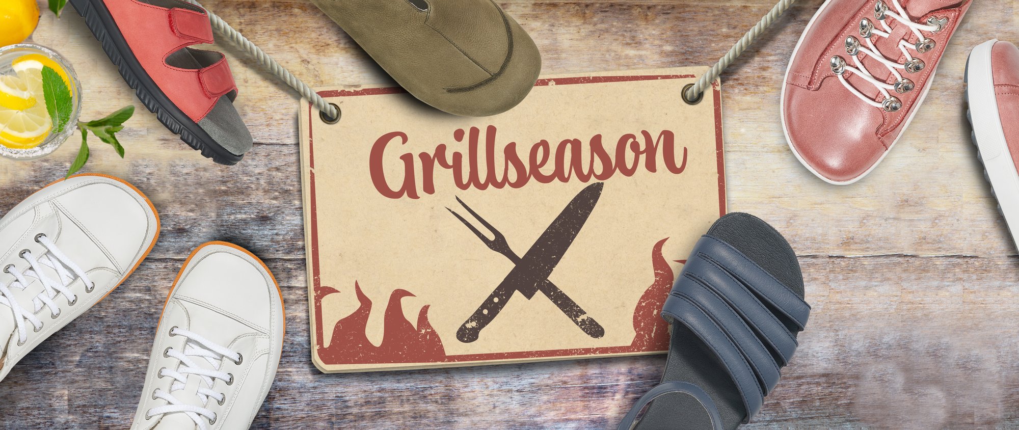 Footwear Display for Grill Season Sale A variety of footwear surrounding a sign that says 'Grill Season' on a wooden background, with a lemon drink on the side.