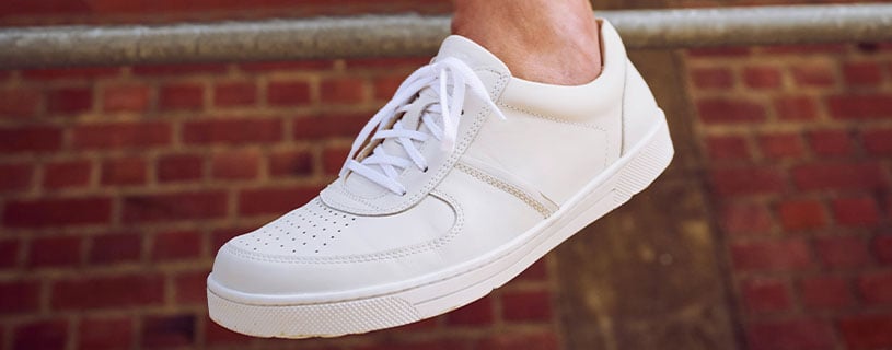Nahaufnahme eines weißen Herren-Sneakers mit perforiertem Design auf rotem Backsteinboden