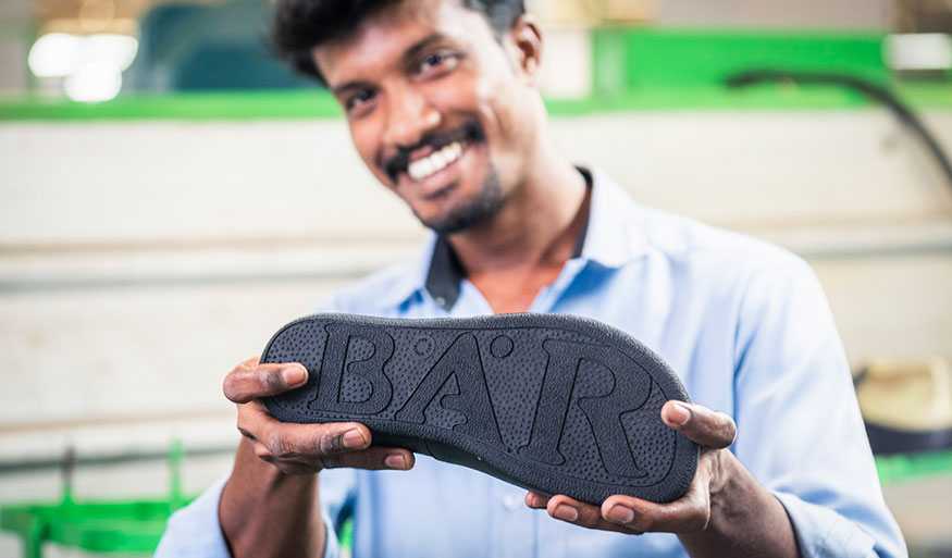 Mann präsentiert Schuhsohle mit BAR-Logo Ein Mann in einem blauen Hemd hält eine Schuhsohle mit dem Schriftzug BAR in die Kamera