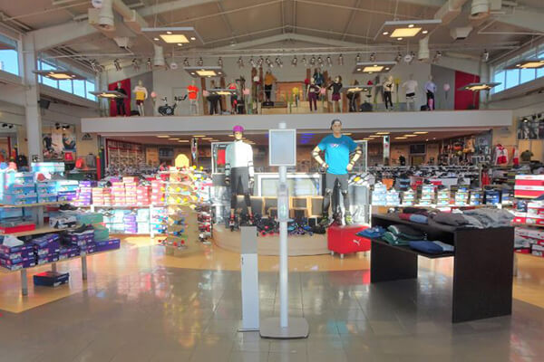 Innenansicht eines großen Sportgeschäfts mit einer Vielzahl von Schuhen, Sportbekleidung und Accessoires auf Regalen und Auslagen.