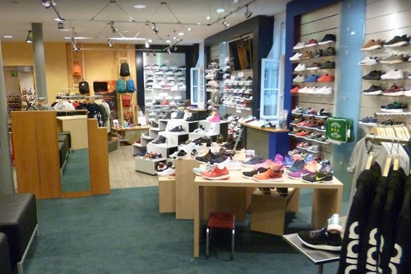 Innenansicht eines Sportbekleidungsgeschäfts mit zahlreichen Sportschuhen und Kleidung auf Regalen und Tischen.