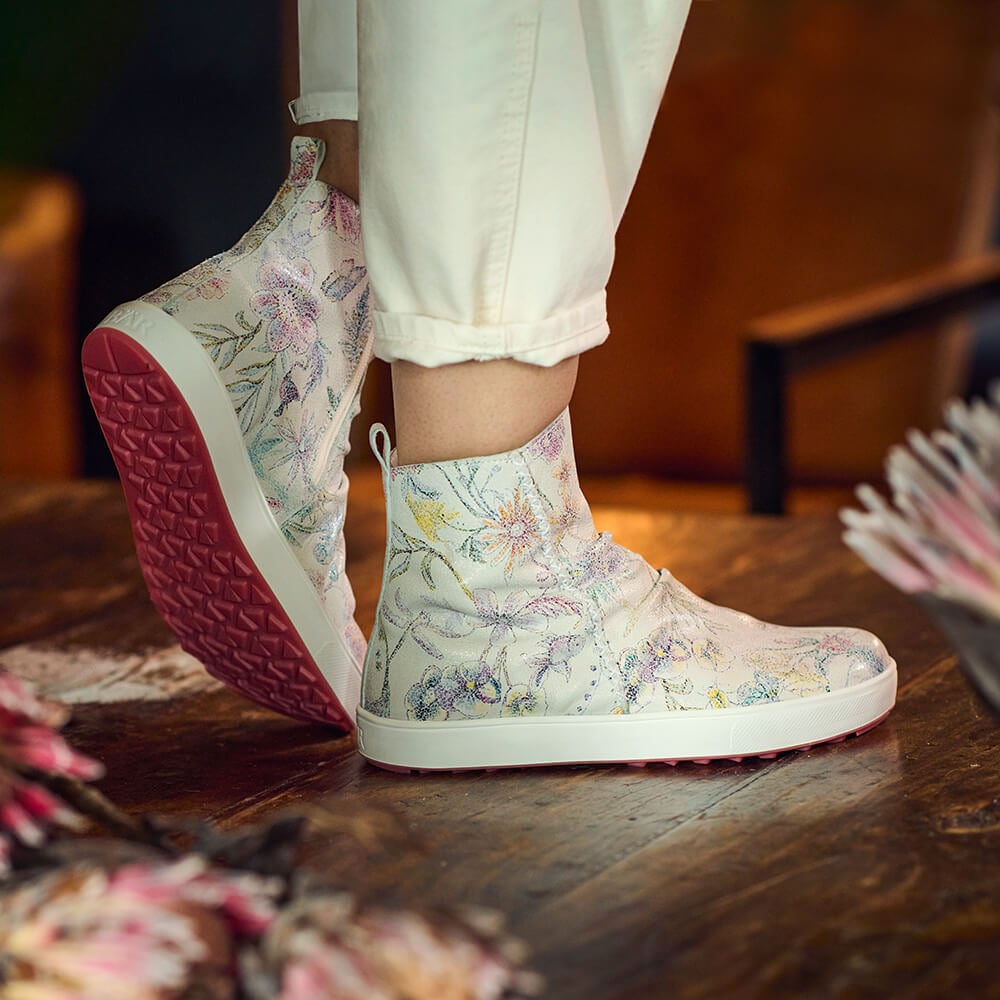 Person wearing floral ankle boots with pink soles on a wooden floor