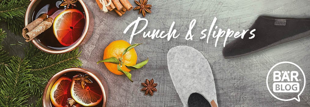 Cozy Winter Essentials: Warm Punch and Comfortable Slippers Two cups of spiced punch with citrus slices and a pair of cozy slippers on a festive table setting.