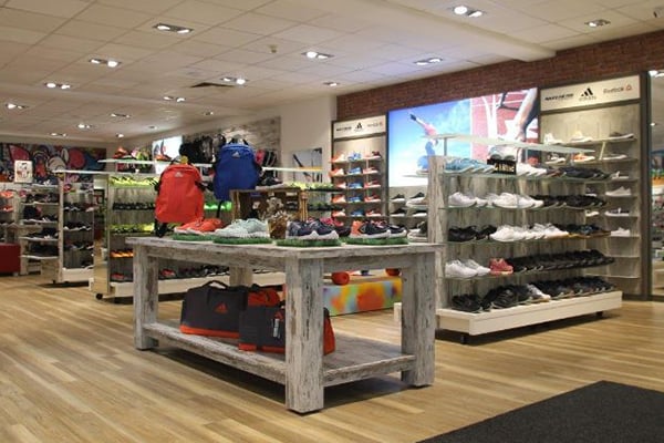 Ein gut beleuchteter Sportladen präsentiert eine breite Auswahl an Sportschuhen und Taschen auf Holzregalen.