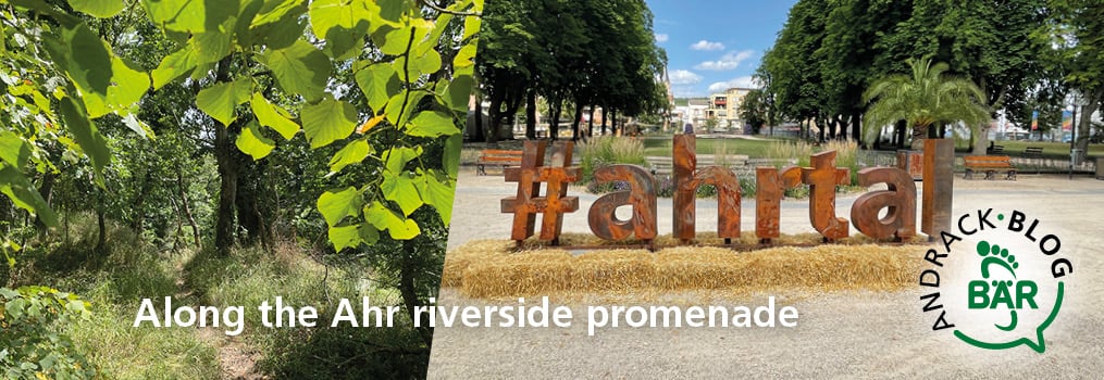 Lush green trees lining the Ahr riverside promenade with a large '#ahrtal' sign and sunny blue skies.