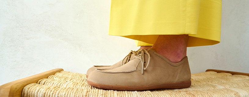 Close-up of beige moccasins paired with yellow trousers on a woven surface