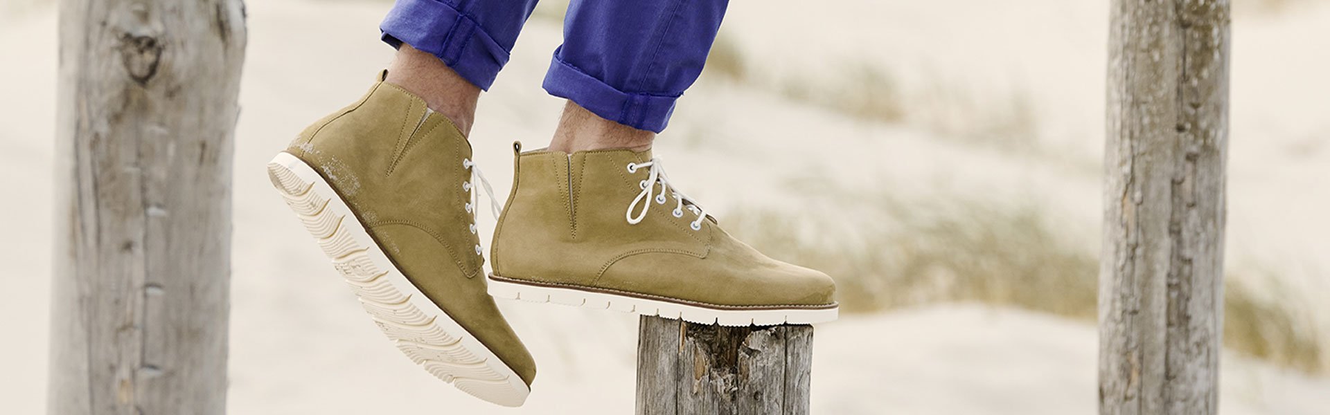 Modische beige Stiefel mit weißer Sohle an einer Person, die auf Holzpfählen balanciert. Beige Stiefel mit weißer Sohle auf Holzpfählen, getragen von einer Person in blauer Hose.