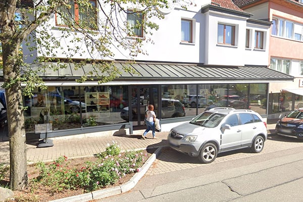 Modernes Geschäftshaus mit Glasfassade, Auto auf Parkplatz, Passant auf Gehweg