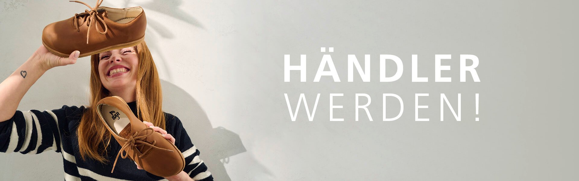 Lächelnde Frau hält handgefertigte Schuhe; Text 'Händler werden!' im Bild