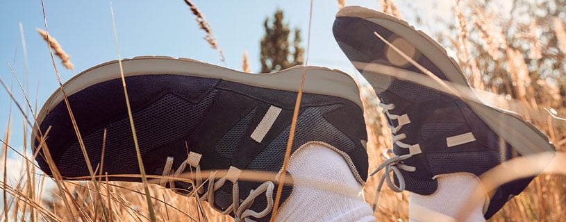 Schwarze Sneakers auf einer Wiese mit trockenem Gras im Herbst