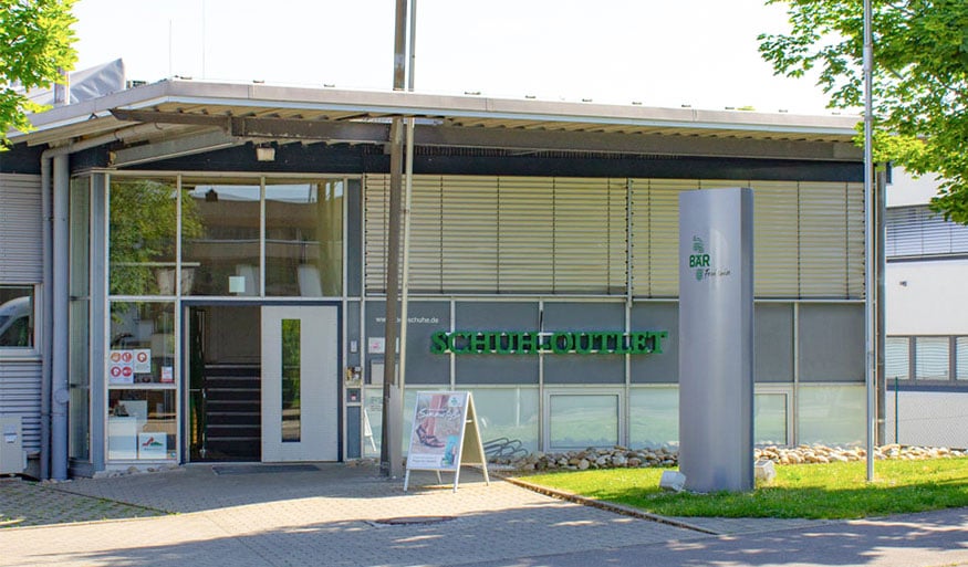 Eingang eines Schuhoutlets mit moderner Glasfassade Eingangsbereich eines Schuhoutlets mit großen Glasfenstern und einem grünen Schild über der Tür.