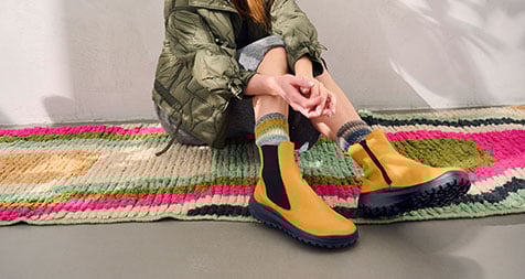 Modische gelbe Chelsea-Boots mit bunter Sohle Frau in gelben Chelsea-Boots auf buntem Teppich sitzend