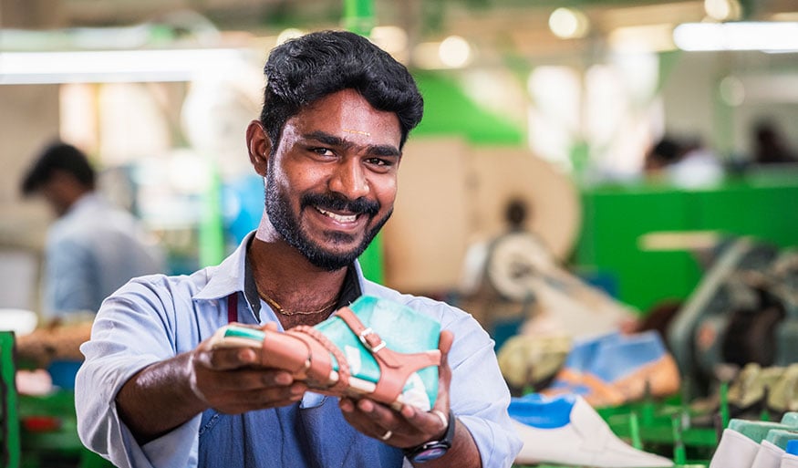 Freundlicher Arbeiter in Schuhfabrik präsentiert fertigen Schuh Ein lächelnder Mann in einer Fabrik zeigt stolz einen hergestellten Schuh.