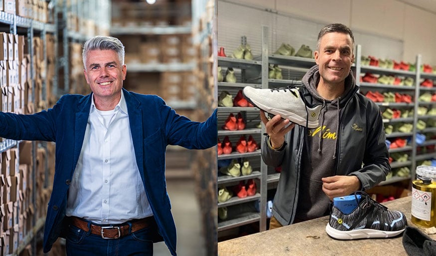 Zwei Männer in einem Lager mit Schuhen: links ein Mann in einem blauen Anzug vor Regalen mit Kartons, rechts ein Mann in dunkler Kleidung hält einen Schuh. Links ein Mann in einem Anzug in einem Lager mit Kartons, rechts ein Mann in dunkler Kleidung mit einem Schuh in der Hand, im Hintergrund Regale mit Schuhen.