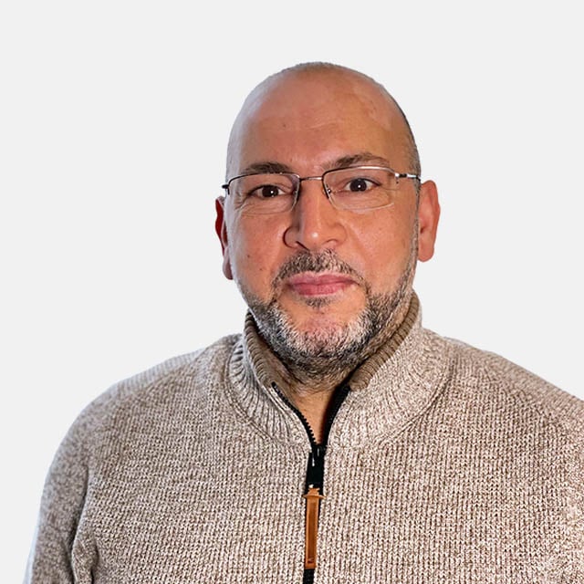 Porträt eines Mannes mit Brille in einem beigen Pullover Ein Mann trägt eine Brille und einen beigen Pullover mit Reißverschluss, vor einem neutralen Hintergrund