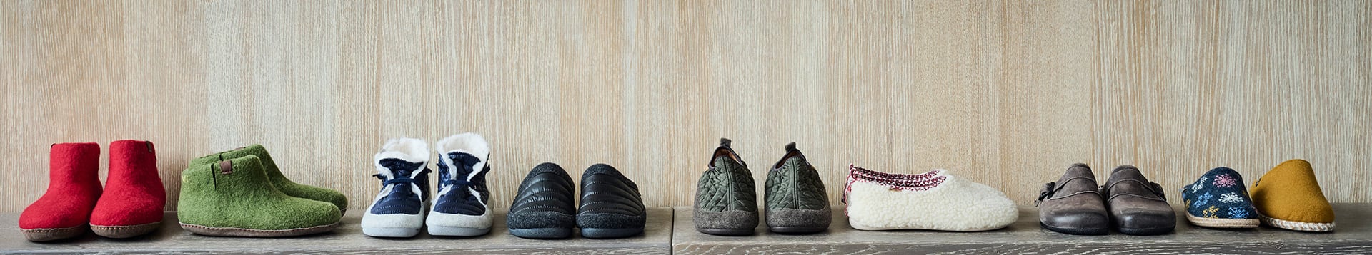 Collection of Winter Slippers in Various Colors and Designs A variety of winter slippers displayed on a wooden surface, including red, green, blue, black, and patterned designs.