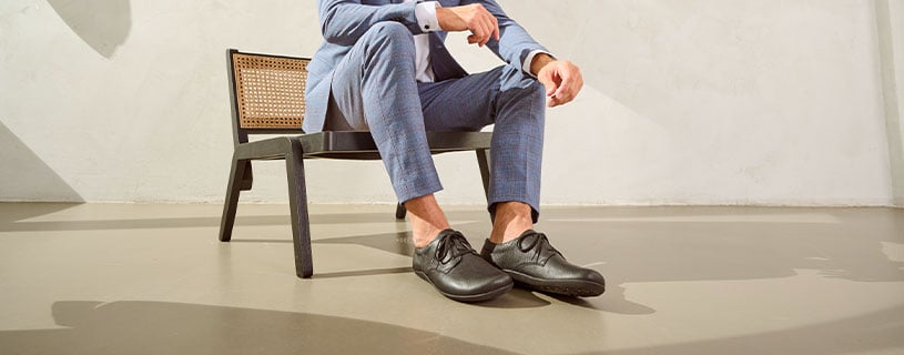 Man sitting on a chair wearing a blue suit and black dress shoes, showcasing a modern and stylish look.
