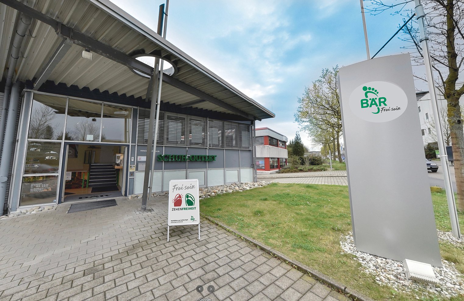 Außenansicht des Schuh-Outlet-Gebäudes mit Werbeschild von BÄR Schuh-Outlet-Gebäude mit BÄR-Werbeschild und Eingang in grüner Umgebung