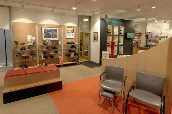 Innenansicht eines Schuhgeschäfts mit modernen Regalen und Sitzgelegenheiten Ein Schuhgeschäft mit modernen Regalen voller Schuhe, roten Sitzbänken und grauen Stühlen auf rotem Teppichboden.