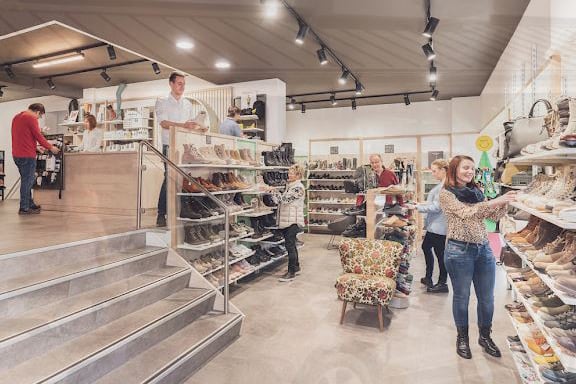 Menschen beim Stöbern in einem gut besuchten Schuhgeschäft mit Regalen voller Schuhe und Handtaschen.